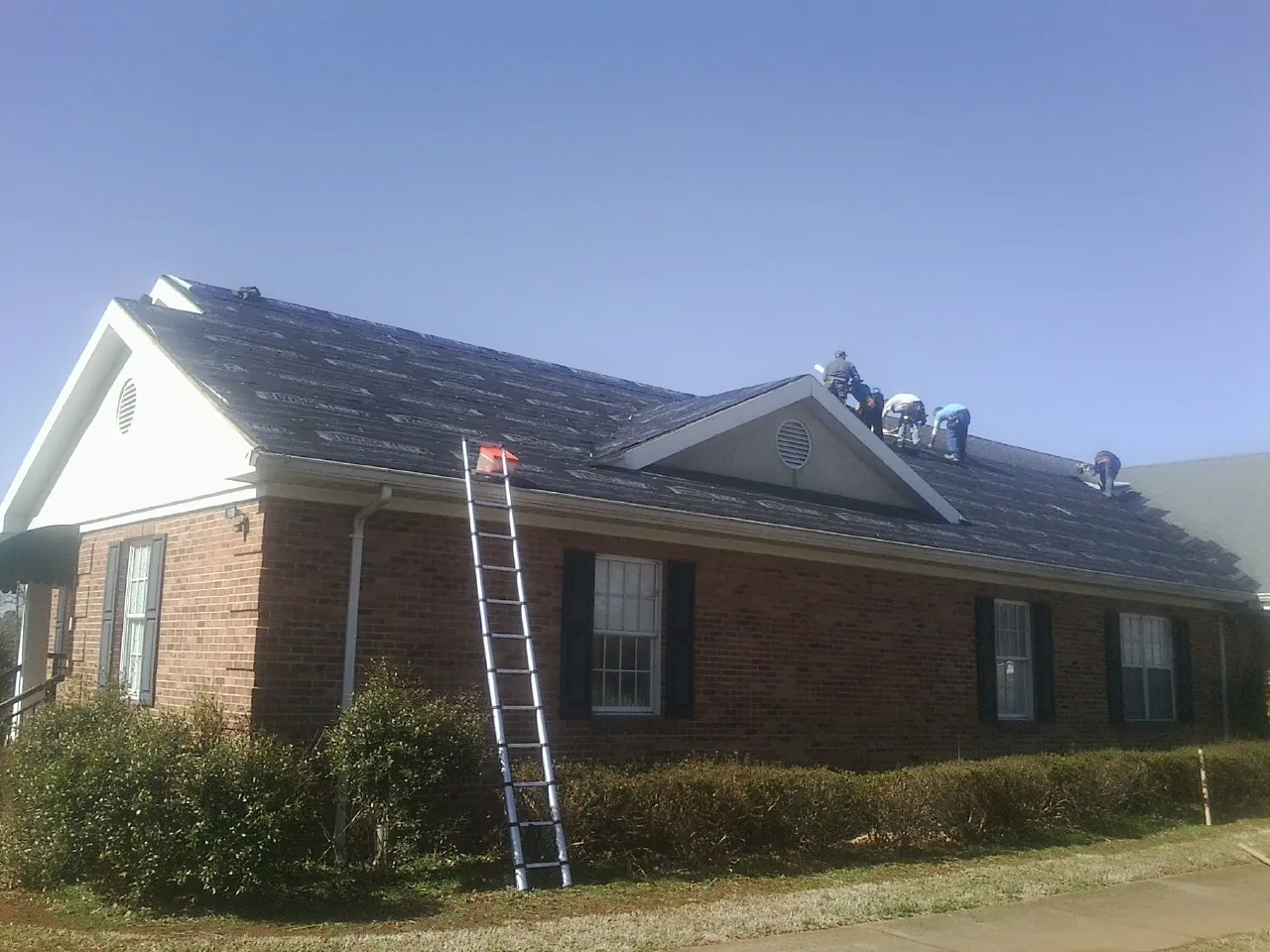 Crew tearing shingles off a brick ranch roof with a ladder set — Emergency Roof Repair work by our crew in Circleville